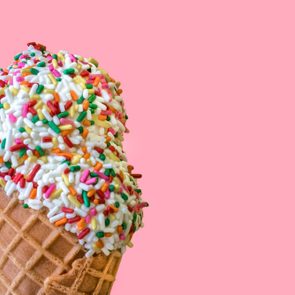 Ice Cream Scoops with Colored Sprinkles in a Waffle Cone on a Light Pink Background