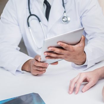 Checking medical tests. Serious doctor and patient. Doctor holding tablet and talking with a patient in the hospital. Close-up view of the hands and the tablet.