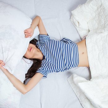 Girl sleeps in a white bed at home. Young woman sleeping in sleepwear on the white linen in bed at home, top view.