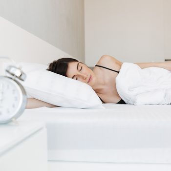 Portrait of a beautiful young woman sleeping in bed at the bedroom with alarm clock on a nightstand