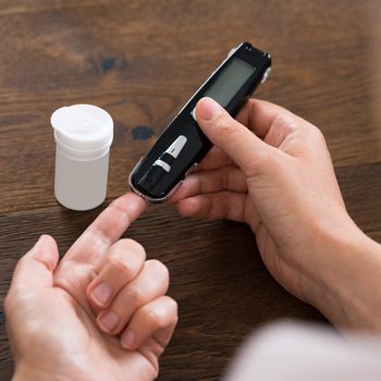 Close-up Of Person Hands Holding Glucometer For Measuring Blood Sugar At Desk