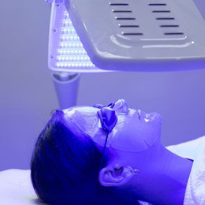 Young woman having blue LED light facial therapy treatment in beauty salon. Beauty and wellness