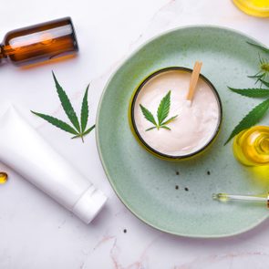 Cosmetics with cannabis oil on a turquoise plate on a light marble background. Copy space, mockup.