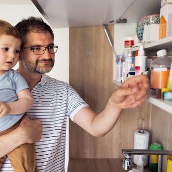 man holding his son while grabbing something from the medicine cabinet at home