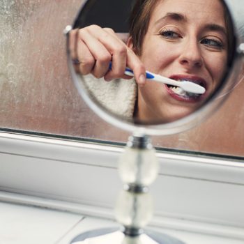 Woman looking in the mirror brushing her teeth