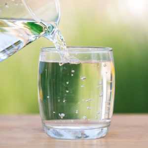 pouring water from a clear glass pitcher into a clear glass cup