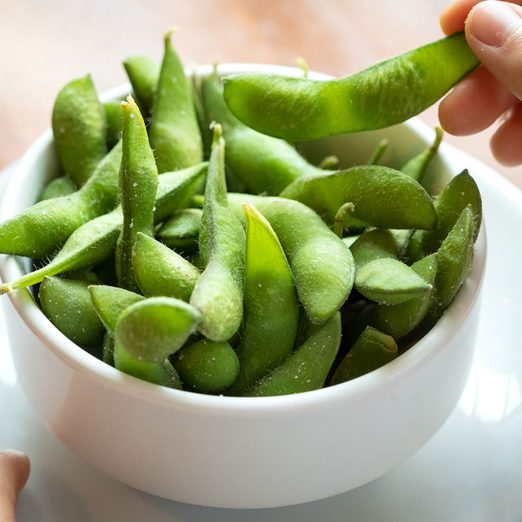 close up view of a hand grabbing some edamame from a bowl at a wood table in a restaurant